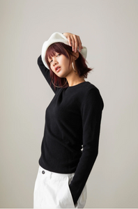 Person wearing a black long-sleeve top and white pants against a plain background