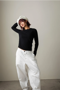 Person wearing a black top and white pants against a plain background