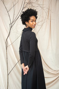 Woman wearing a black dress standing against a beige curtain with branches.