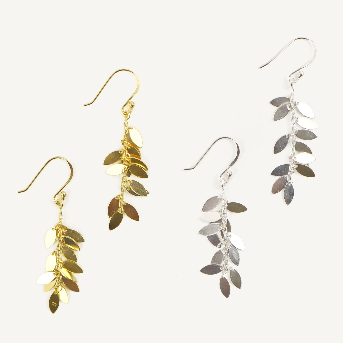 Two pairs of leaf-shaped earrings, one gold and one silver, on a white background.
