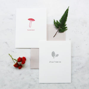 Greeting cards with illustrations of a mushroom and a fern on a marble surface.