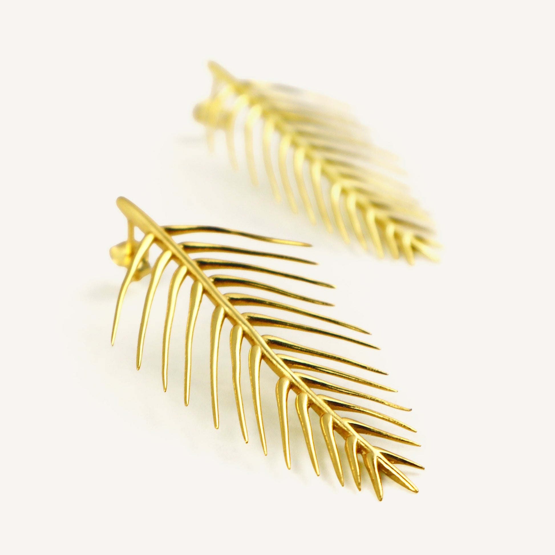 Gold leaf-shaped earrings on a light beige background