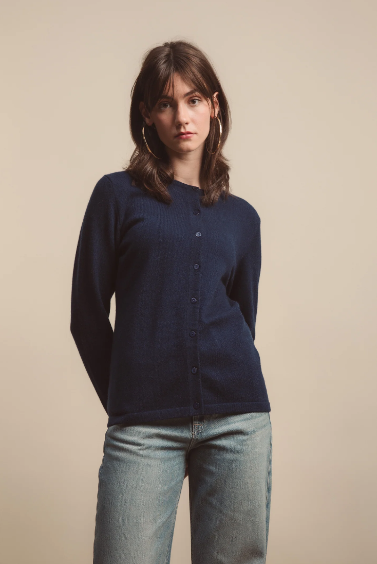 Woman wearing a navy cardigan and light blue jeans against a beige background