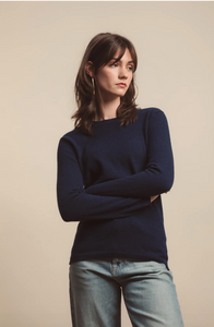 Woman wearing a navy sweater and light blue jeans against a beige background