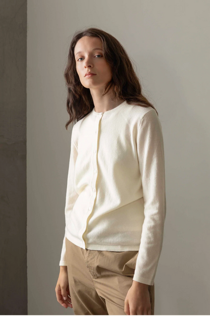 Woman wearing a white long-sleeve shirt and beige pants against a plain background