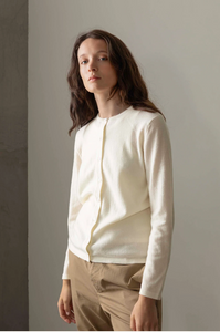 Woman wearing a white long-sleeve shirt and beige pants against a plain background