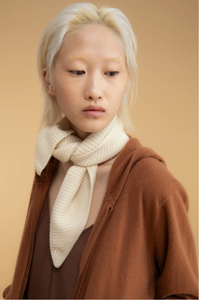 Person wearing a brown coat and white scarf against a beige background