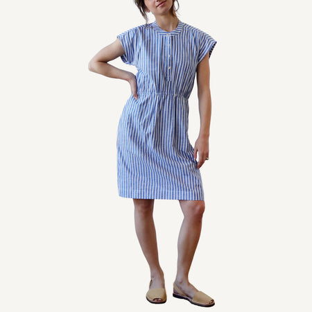 A model wearing a blue striped knee-length dress with short sleeves, elastic waistband, and mother of pearl buttons.
