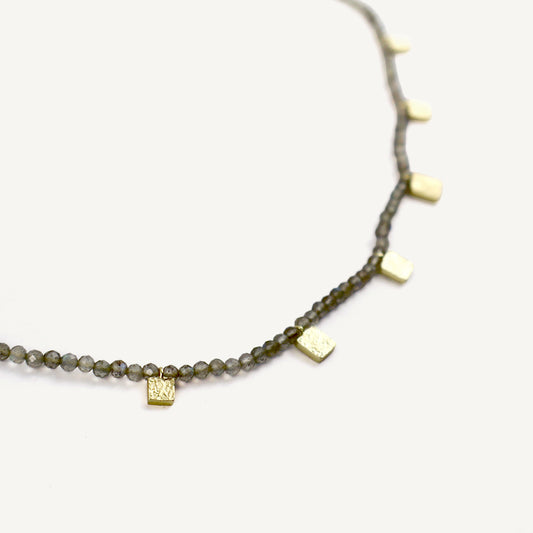 Necklace with green beads and gold square pendants on a white background
