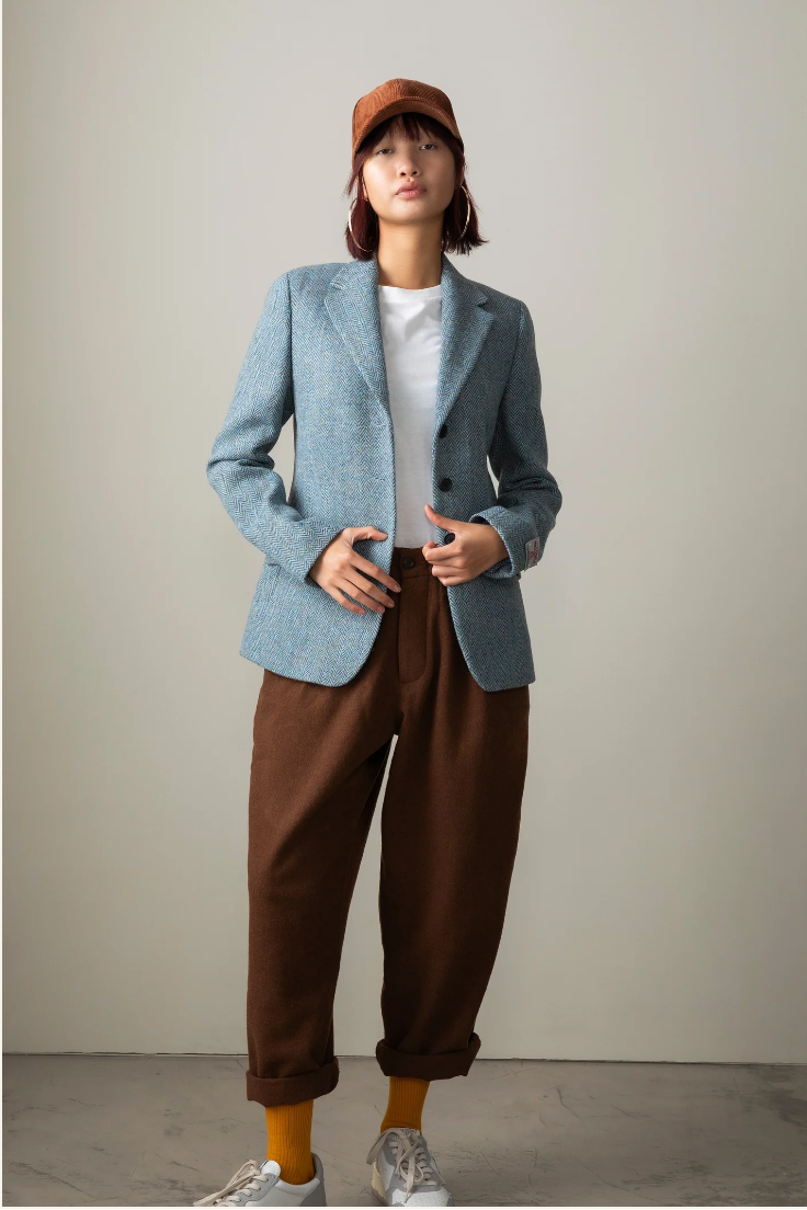 Person wearing a blue blazer, brown pants, and a cap against a plain background