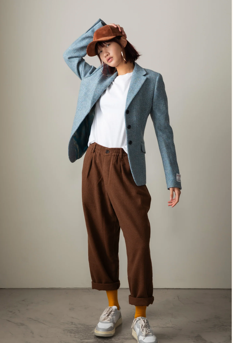 Person wearing a blue blazer, white shirt, brown pants, and a brown hat against a plain background