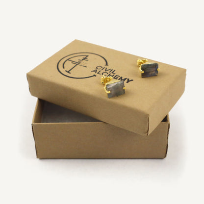 Open cardboard box with earrings on a white background, featuring 'Civil Alchemy' branding.