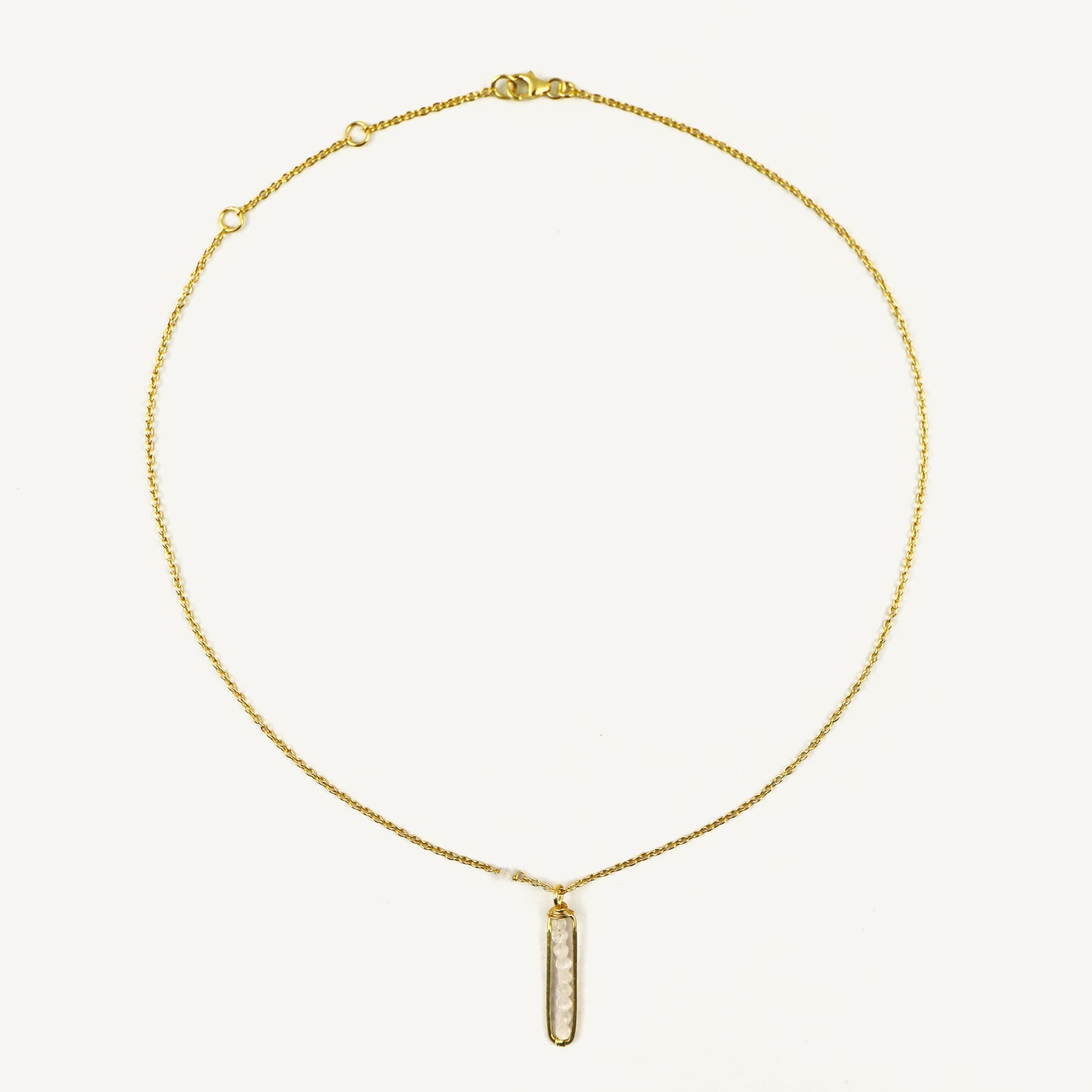 Gold necklace with a vertical pendant on a light beige background