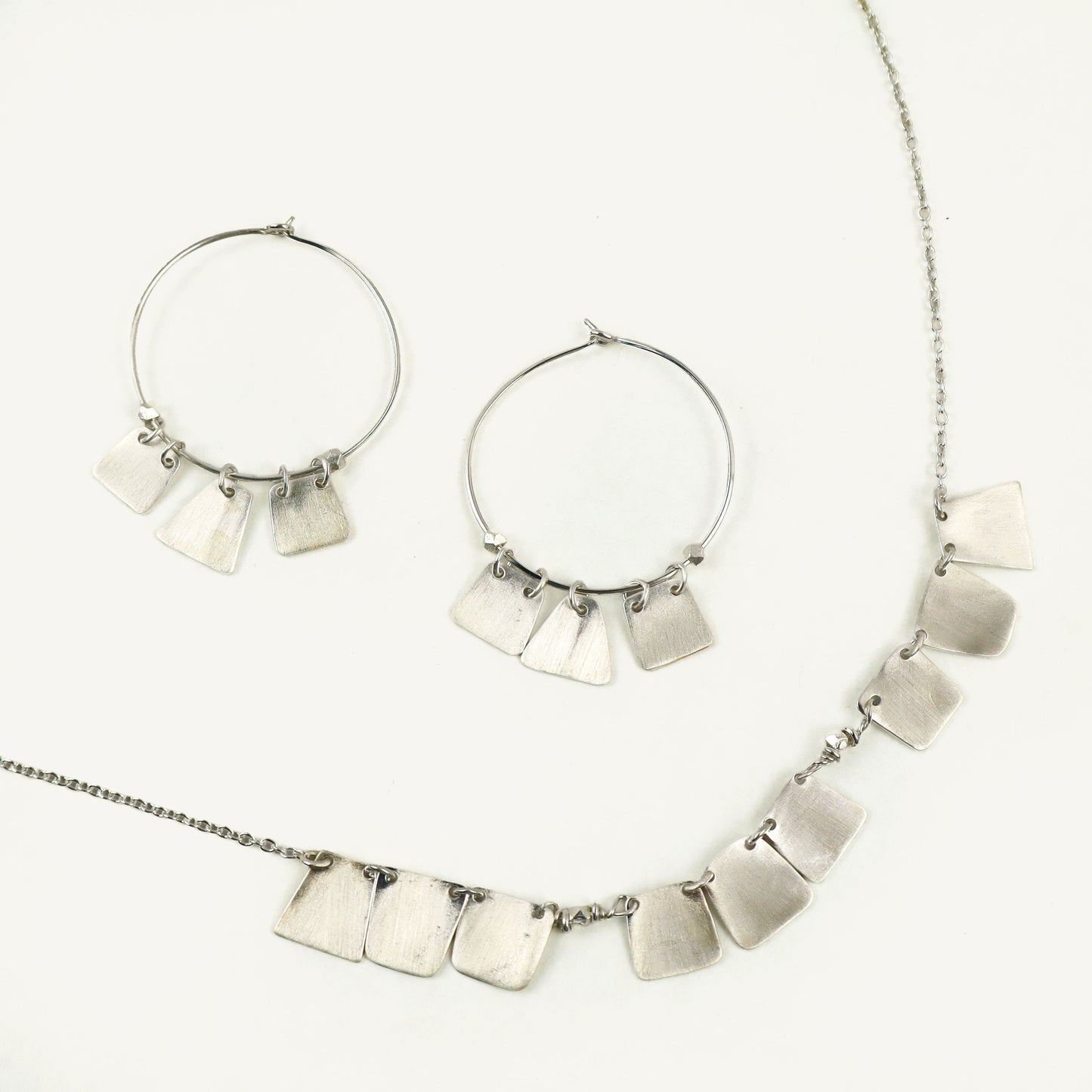 Silver necklace and hoop earrings on a white background