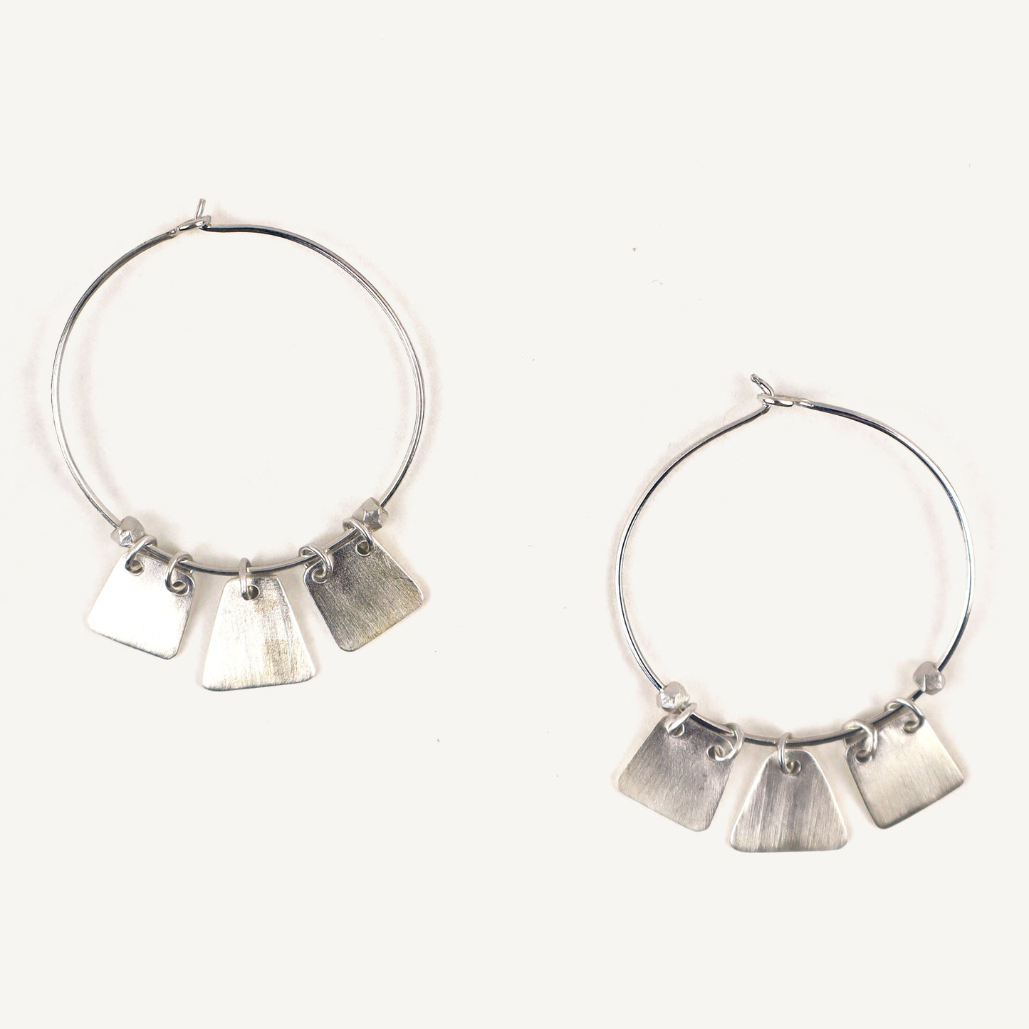 Silver hoop earrings with dangling tags on a white background
