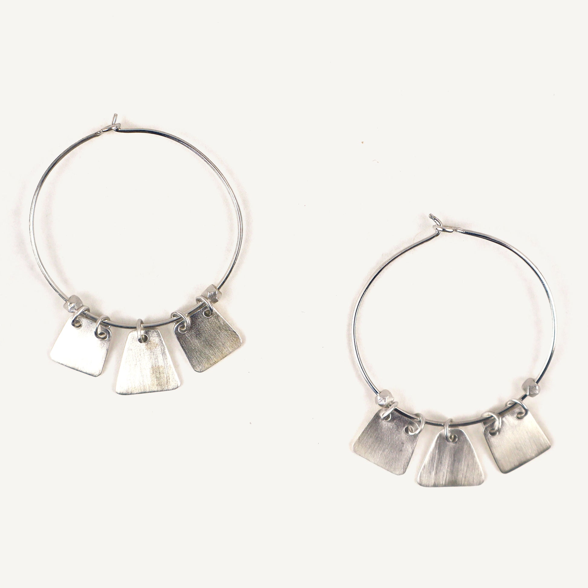 Silver hoop earrings with dangling tags on a white background
