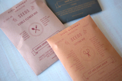 Two packets of Civil Alchemy Seeds on a light surface