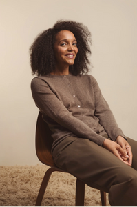 Woman sitting on a chair wearing a brown outfit against a plain background