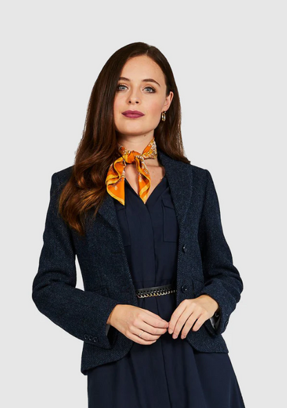 Woman wearing a navy blazer and dress with an orange scarf against a light gray background