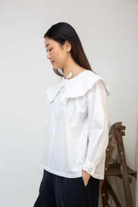 Woman wearing a white blouse with a large bow collar against a plain background