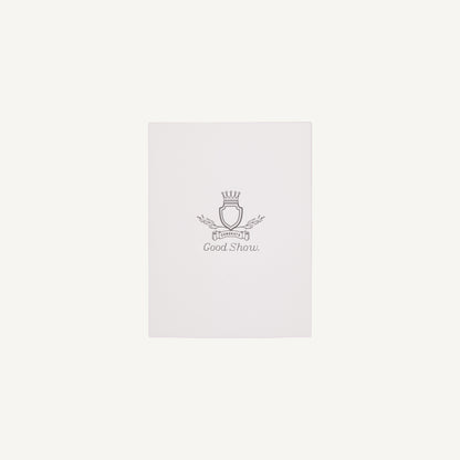A white letterpress congratulations card with a small decorative emblem and text on the front, placed on a clear background.
