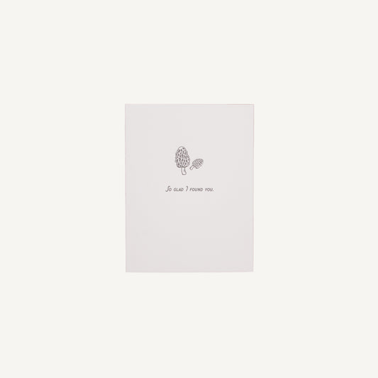 A white letterpress card with a floral design and the text 'So Glad I Found You' on it, placed against a plain background.