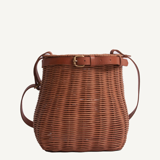 A brown wicker foraging basket with brass hardware and adjustable straps.