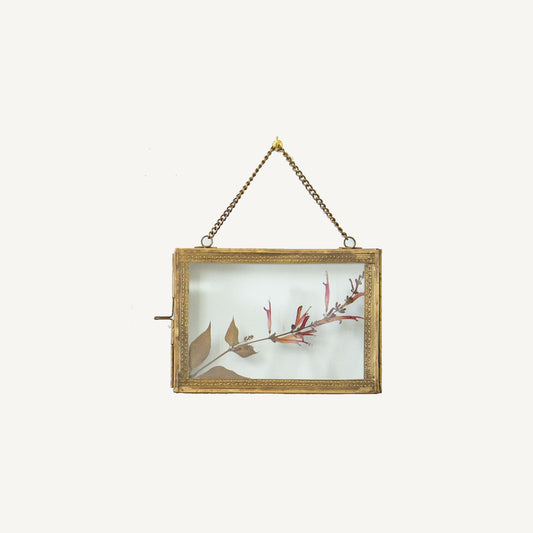 A brass hanging photo frame with a 5x7 dimension, featuring a floral design within the frame, displayed against a plain background.
